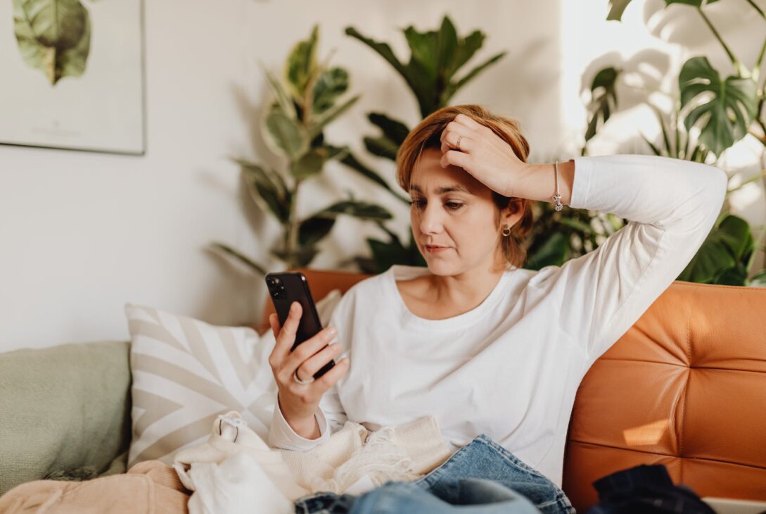 woman sitting on sofa looking at phone and scratching her head