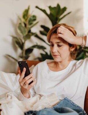 woman sitting on sofa looking at phone and scratching her head