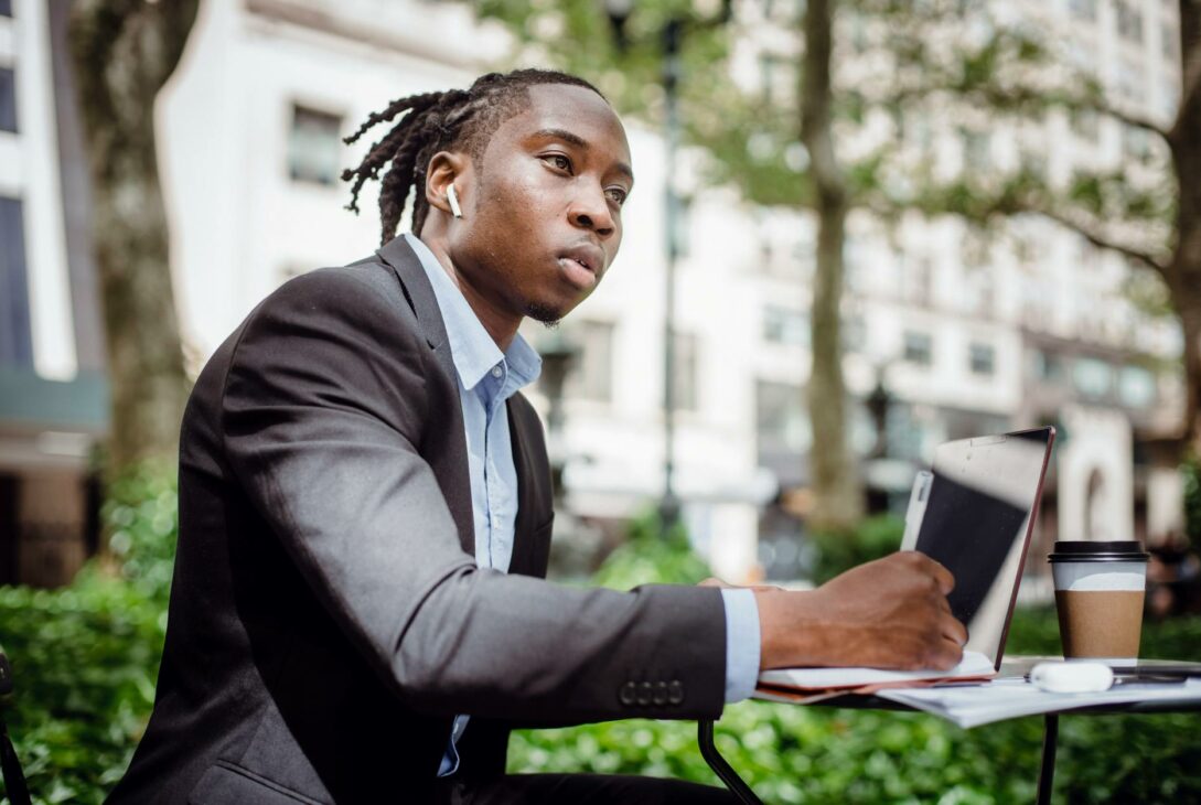 thoughtful black man writing in notebook sitting at table in outdoor cafeteria