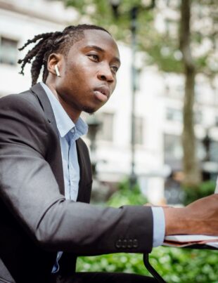 thoughtful black man writing in notebook sitting at table in outdoor cafeteria