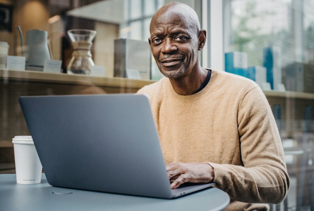 smiling middle aged black man working remotely on netbook in cafe