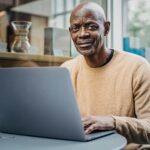 smiling middle aged black man working remotely on netbook in cafe