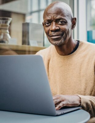 smiling middle aged black man working remotely on netbook in cafe