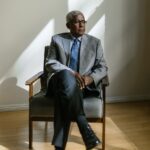 an elderly man in gray suit sitting on a wooden armchair