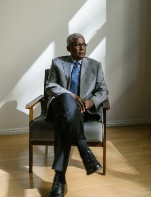 an elderly man in gray suit sitting on a wooden armchair