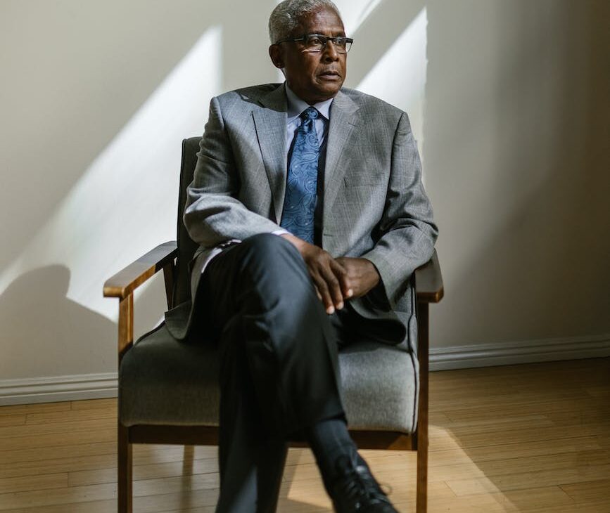 an elderly man in gray suit sitting on a wooden armchair