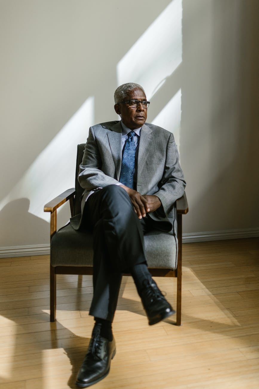 an elderly man in gray suit sitting on a wooden armchair