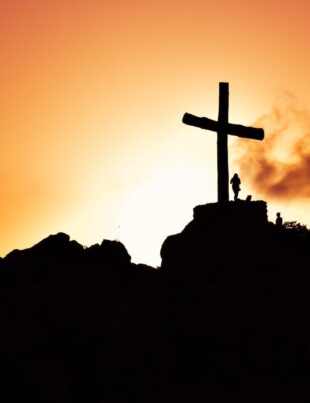 human standing beside crucifix statue on mountain