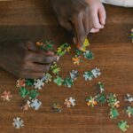 close up shot of two people playing jigsaw puzzle on a wooden surface